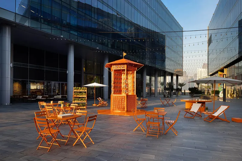 Le Monde d’Hermès kiosk in Dubai Design District at dusk, with orange tables and chairs